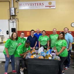 A group of people in green shirts standing in front of a bin at a food bank.