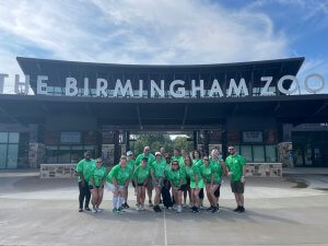 A diverse group of people standing in front of the Birmingham Zoo, showcasing the diverse culture.