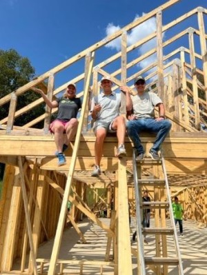 Three people from different cultures sitting on the top of a house under construction.